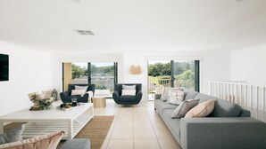 Un salón moderno con un sofá gris, un sillón negro y una mesa de centro blanca. Hay un ventanal con vistas a zonas verdes.