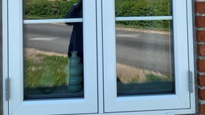 Ventana con marco blanco y vistas despejadas a una carretera, follaje y un edificio al fondo.