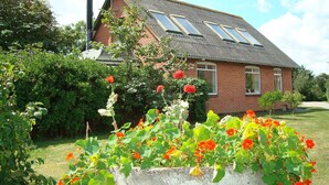 Una casa con techo inclinado, fachada de ladrillo y un jardín con flores rojas.