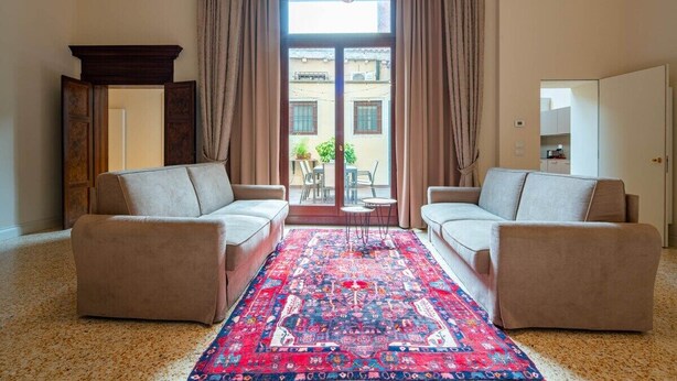 A living room with two sofas, a patterned rug, and a view through a glass door.