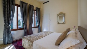 A bedroom with a bed, curtains, a window, and a mirror on the wall.