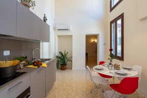 A compact kitchen with modern appliances, a dining area with red chairs, and a potted plant.