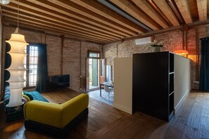 Ein Zimmer mit freiliegenden Backsteinwänden, Holzbalken an der Decke, einem Sofa, einem Esstisch mit Stühlen und einem Kühlschrank.