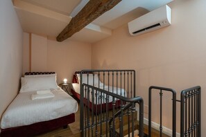 Ein Schlafzimmer mit zwei Betten, einem Holzbalken an der Decke, einer Klimaanlage und einer Treppe mit Metallgeländer.