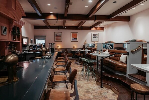 Un restaurante con una barra larga, sillas de madera y un área de estar con sofás y mesas.