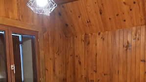 Tunnelmallinen puinen huone, jossa on pyöreä pöytä, kaksi kuviollisilla koristetyynyillä varustettua tuolia, valkoinen, pehmeä matto ja ikkuna, jossa on sälekaihtimet.
