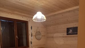 Puinen mökkimainen huone, jossa on kaksi erillistä sänkyä, ikkuna, jossa on sälekaihtimet, seinälle ripustettu peili ja kattovalaisin.