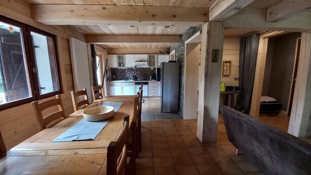 Huoneessa on puinen ruokapöytä tuoleineen, suuri kulho ja sininen alusta. Huoneessa on puulattiat ja korkea katto.