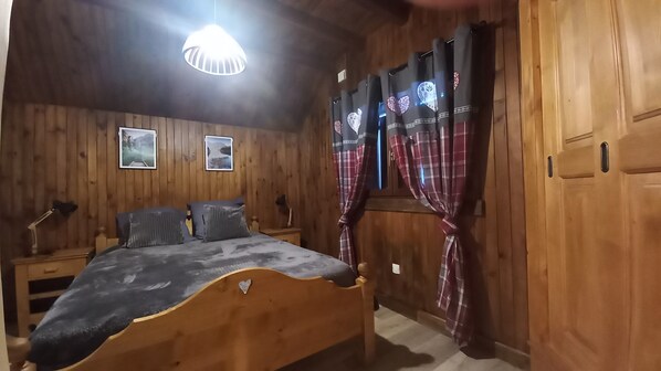 A wooden room with a bed, a desk, and a window with curtains.