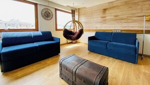 Een moderne woonkamer met twee blauwe banken, een hangstoel, een houten vloer en een groot raam.