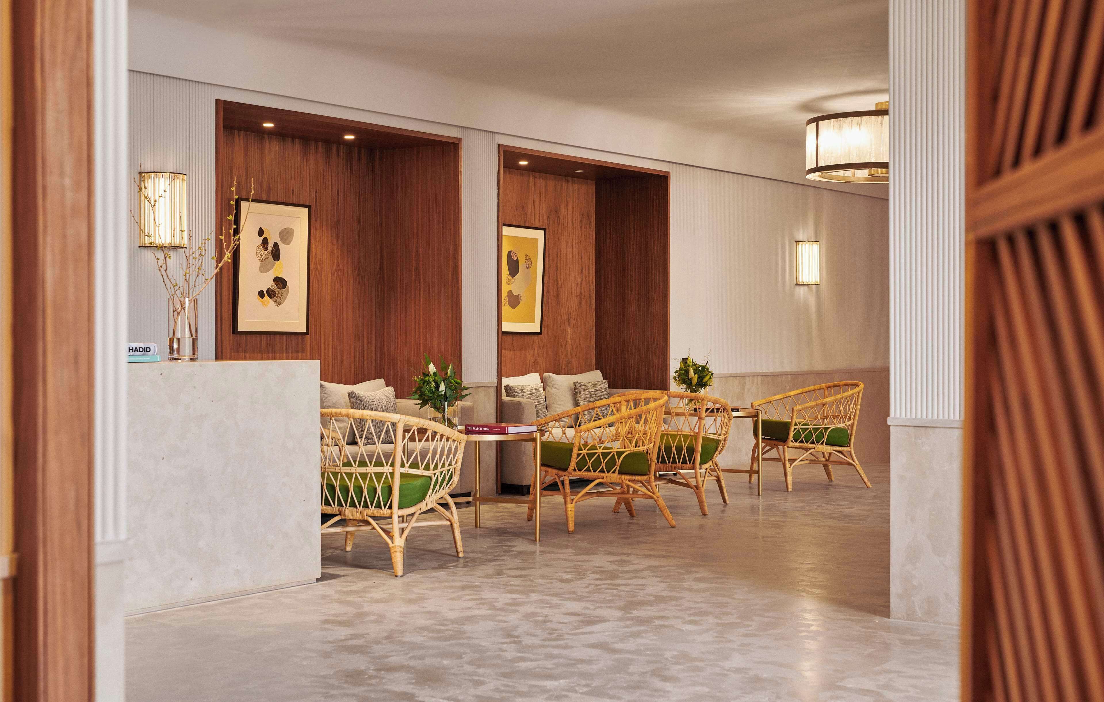 A lobby with a reception desk, wicker chairs, wooden panel walls, and framed artwork.