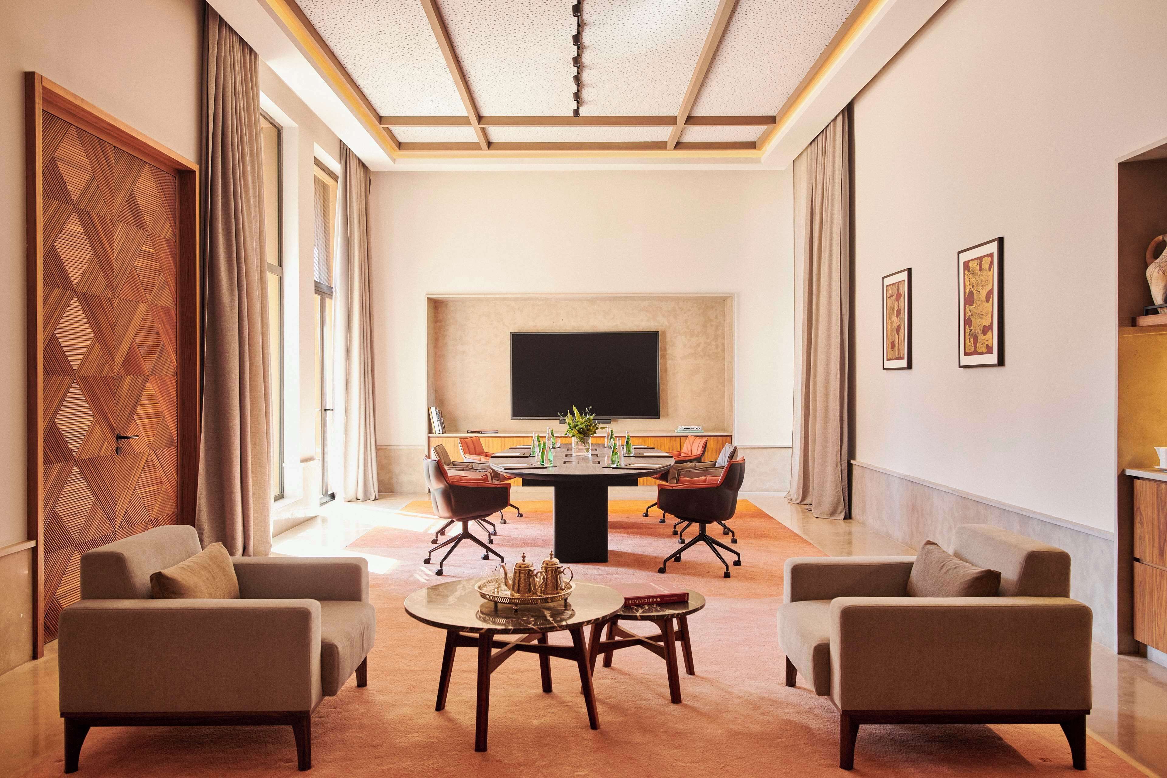 A conference room with a round table, four chairs, and a television screen.