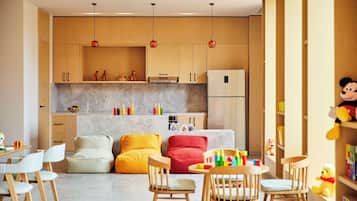 A modern kitchen with wooden cabinets, a refrigerator, and pendant lights. There are colorful pillows and a dining area with chairs.