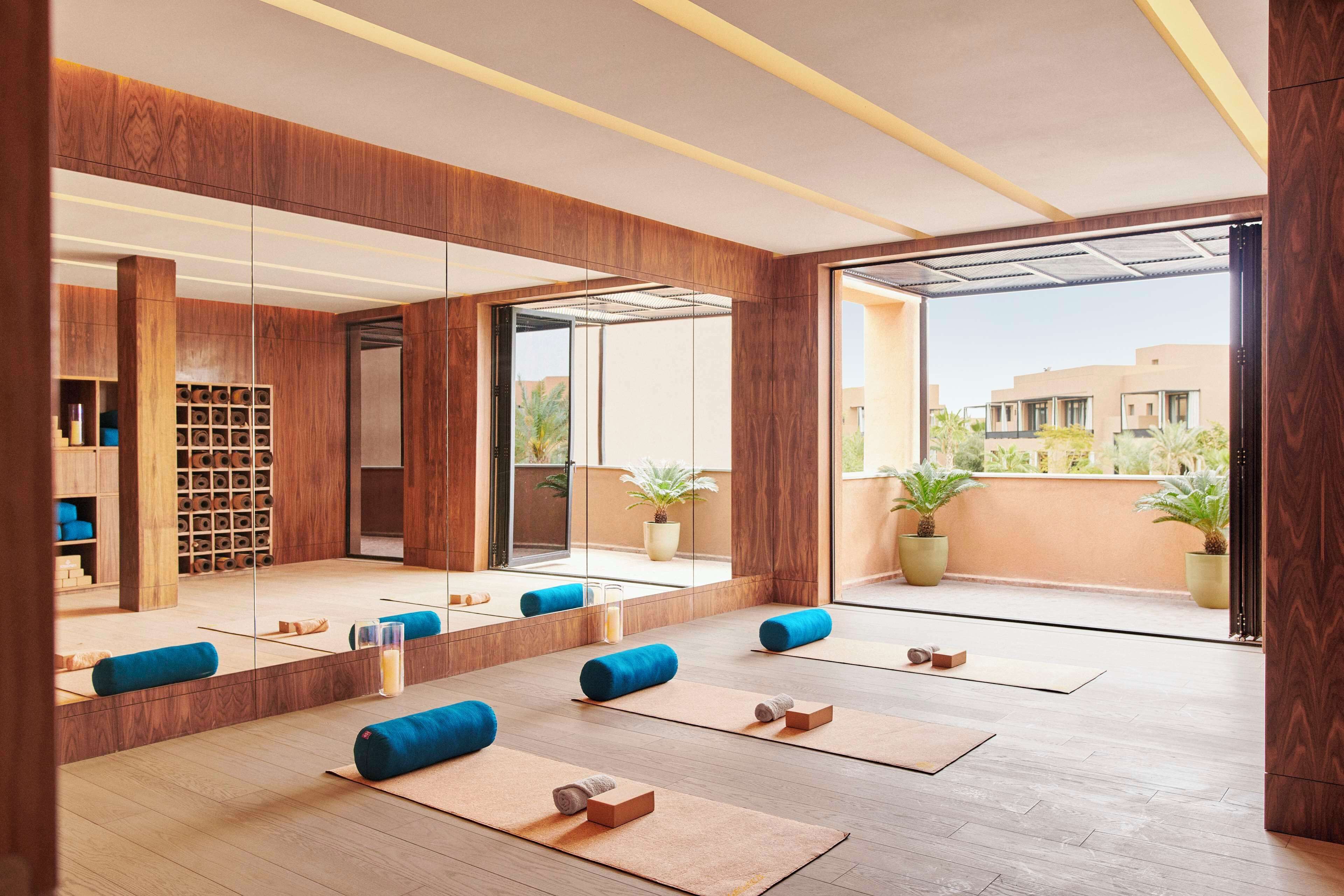 Une pièce spacieuse dotée d’un plancher en bois, de tapis de yoga bleus et d’un grand miroir qui reflète l’ensemble de la pièce.