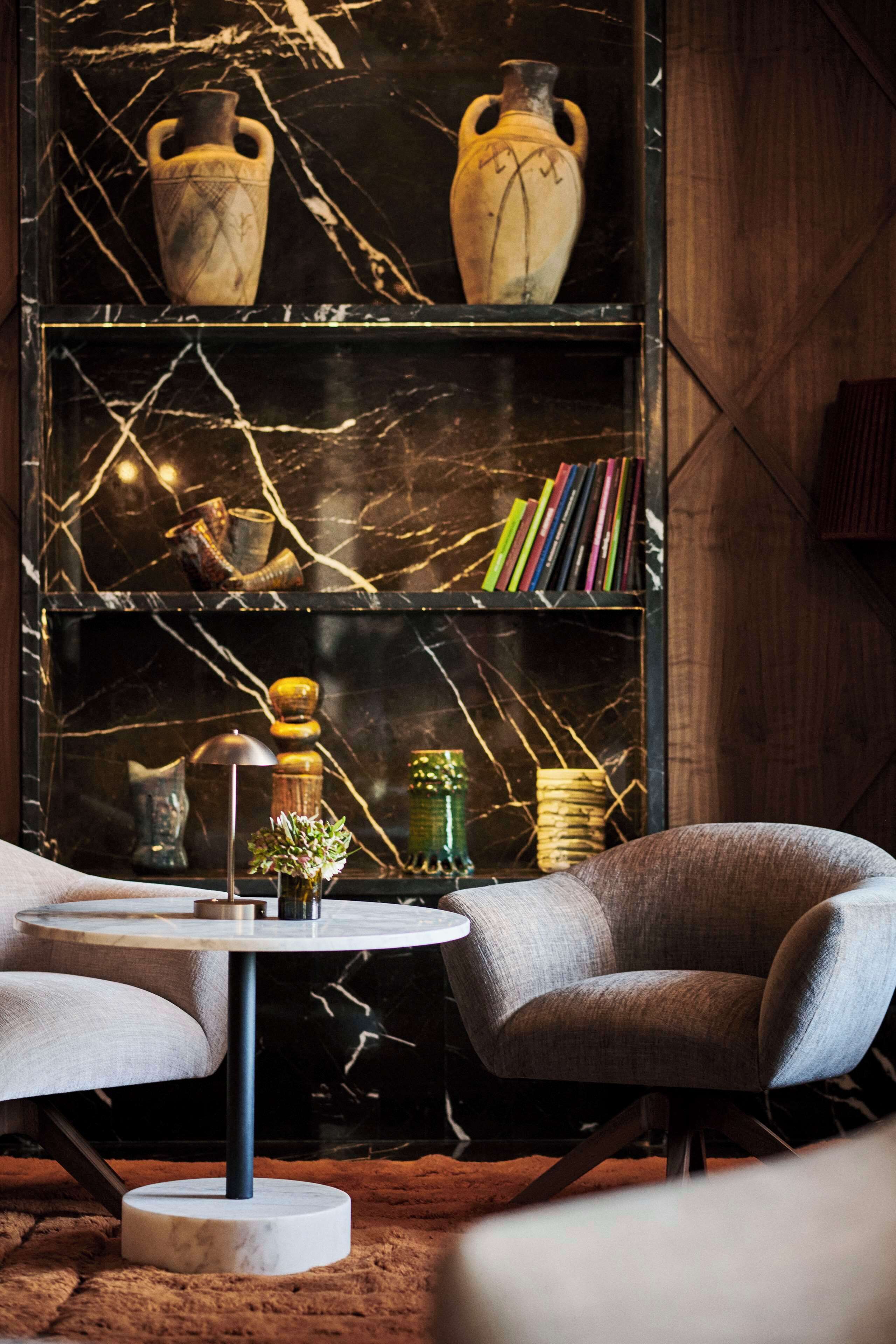 A modern interior with a marble-patterned wall, a bookshelf with books and decorative items, and a round table with a chair.