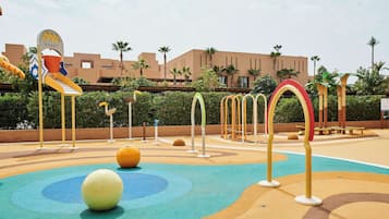 Explore the outdoor play area with a slide and climbing elements, surrounded by a low wall and palm trees.