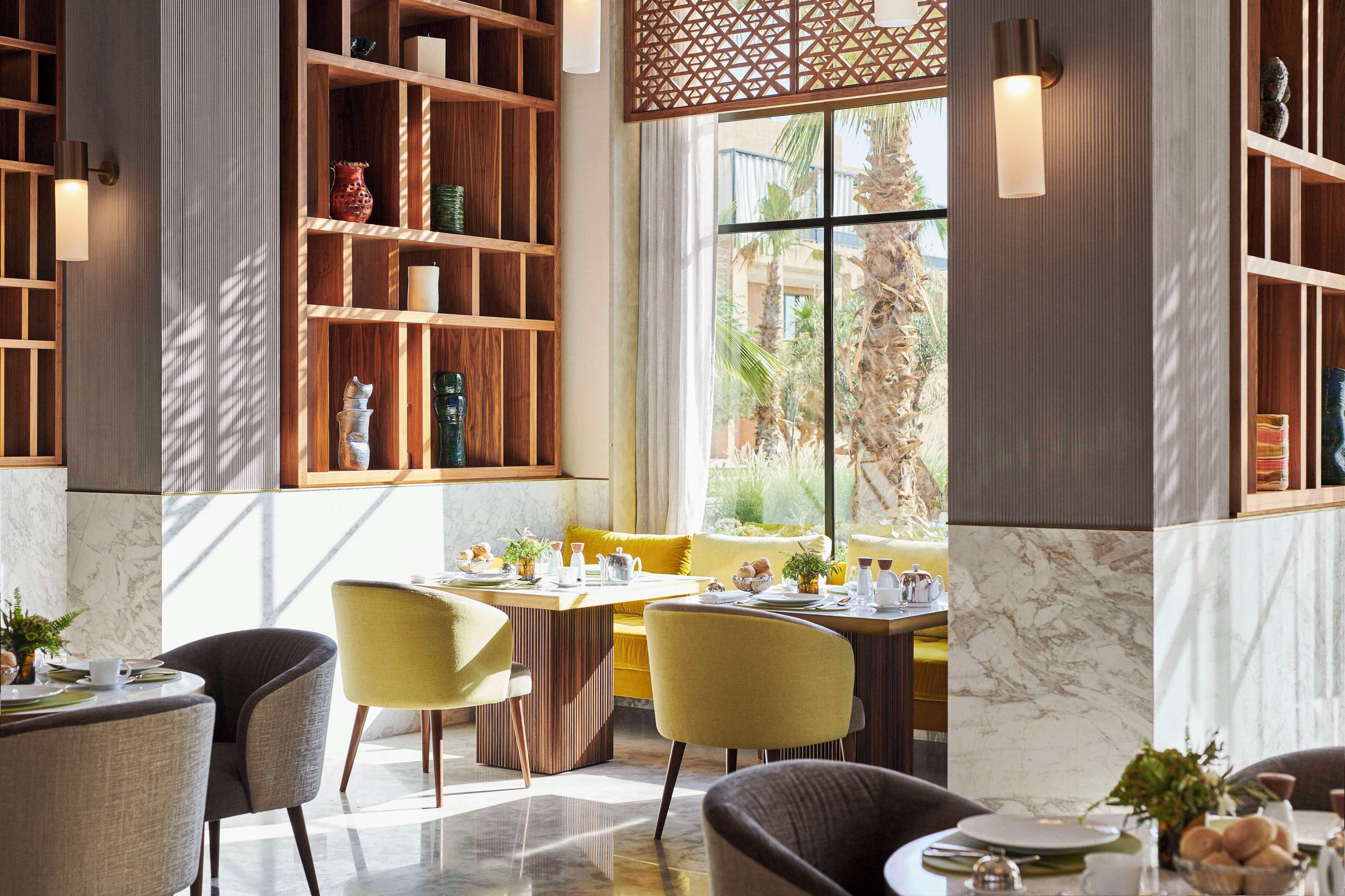 A modern dining area with a wooden bookshelf, a yellow sofa, and a marble floor.