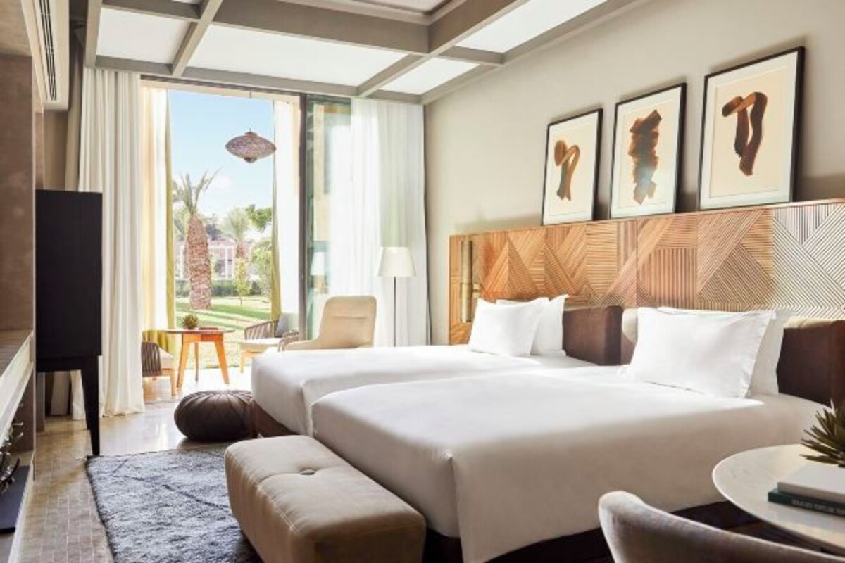 A hotel room with two beds, a TV, a desk, and a view of the outdoors.