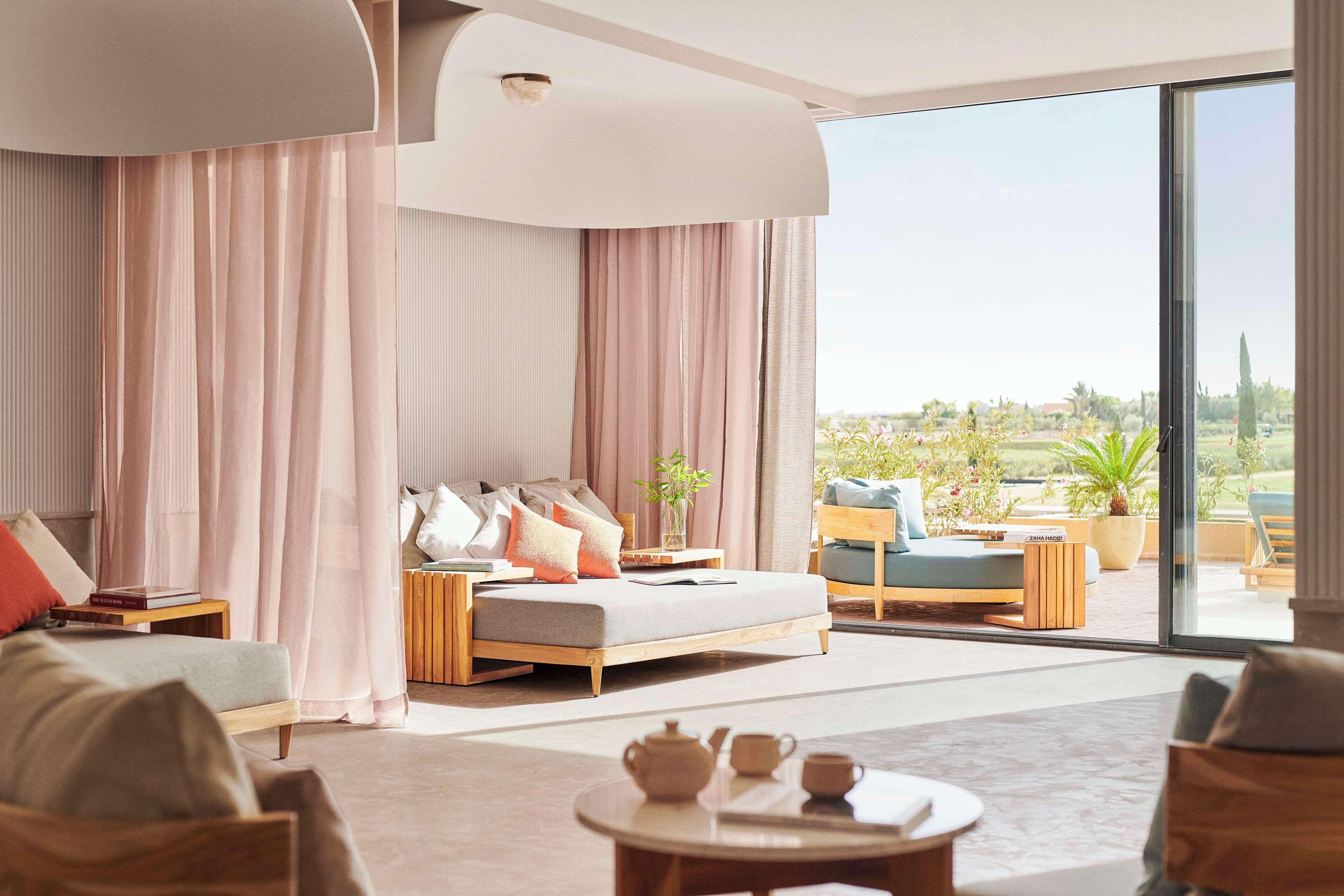A modern bedroom with a large bed, a sofa, a coffee table, and a view of a garden through large windows.