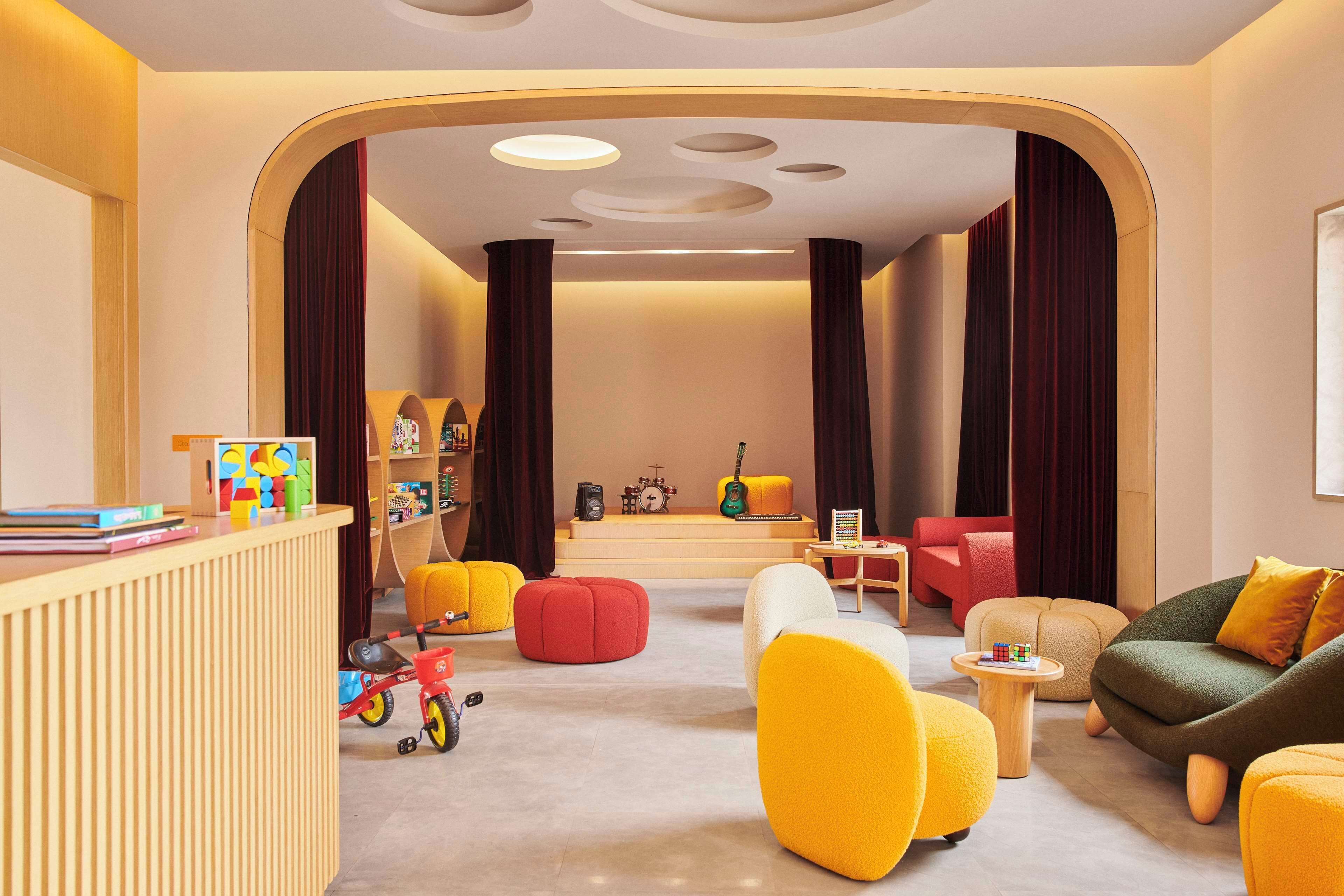 A modern living room with a wooden reception desk, colorful chairs, a small table with a Rubik's cube, and a guitar in the background.