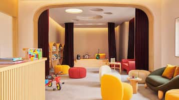 A modern living room with a wooden reception desk, colorful chairs, a small table with a Rubik's cube, and a guitar in the background.