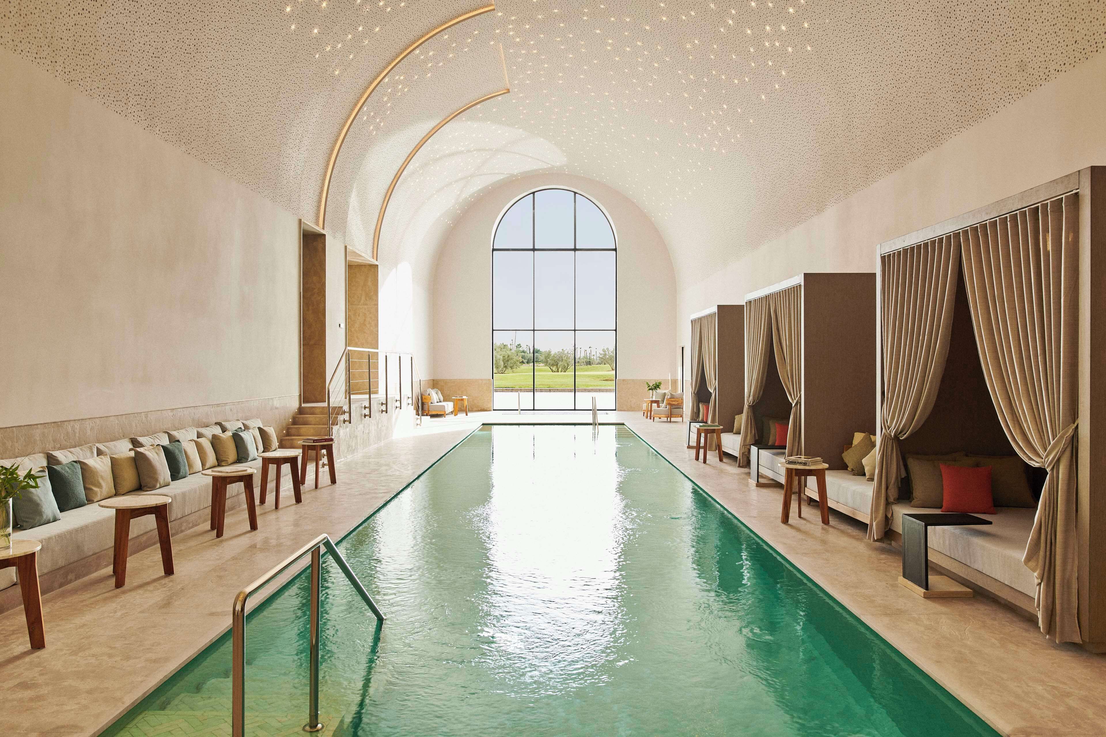 A large indoor swimming pool with a view of the outdoors, surrounded by seating areas and a high ceiling with a starry design.