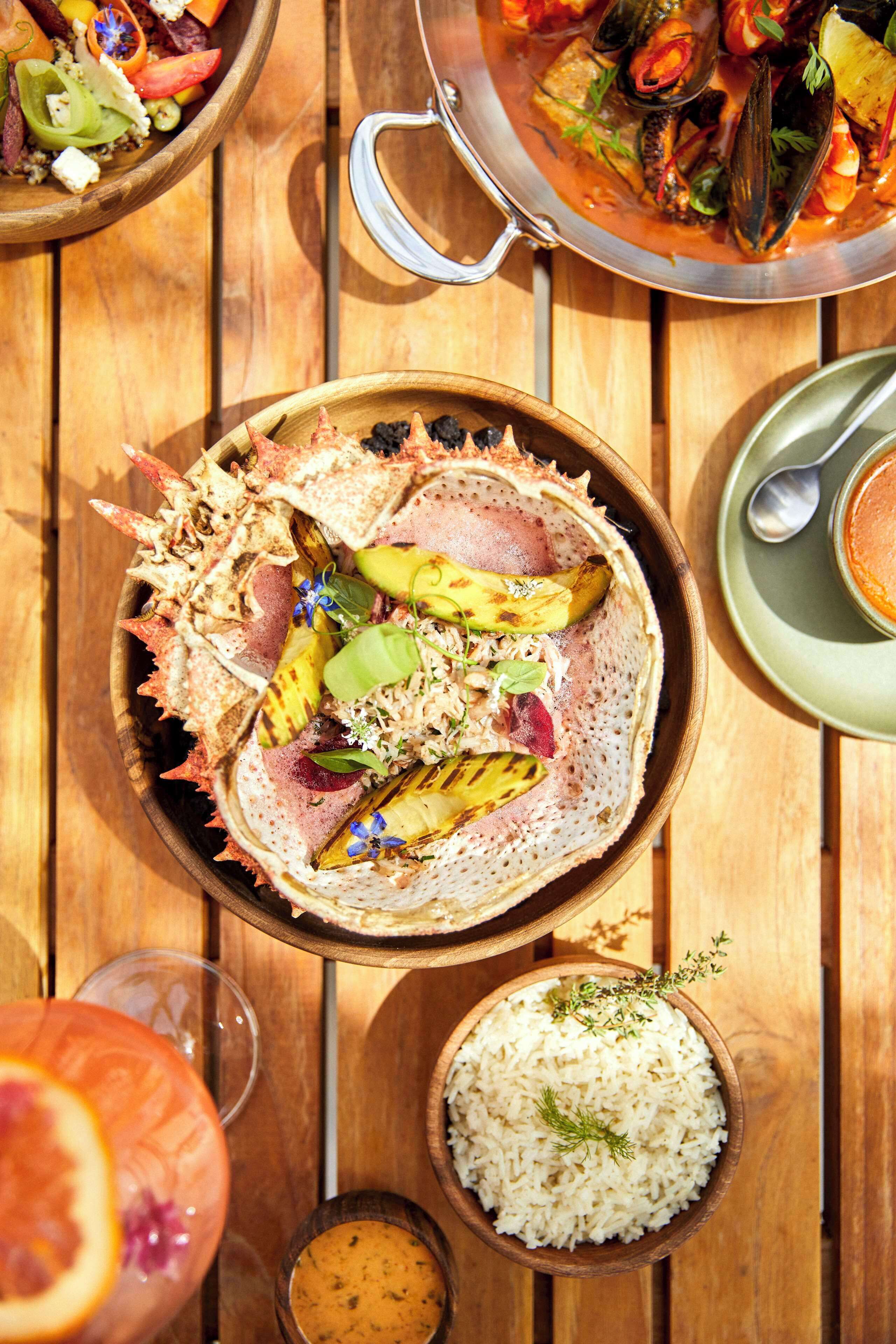 A wooden table with a seafood dish, a bowl of rice, and a glass of drink.