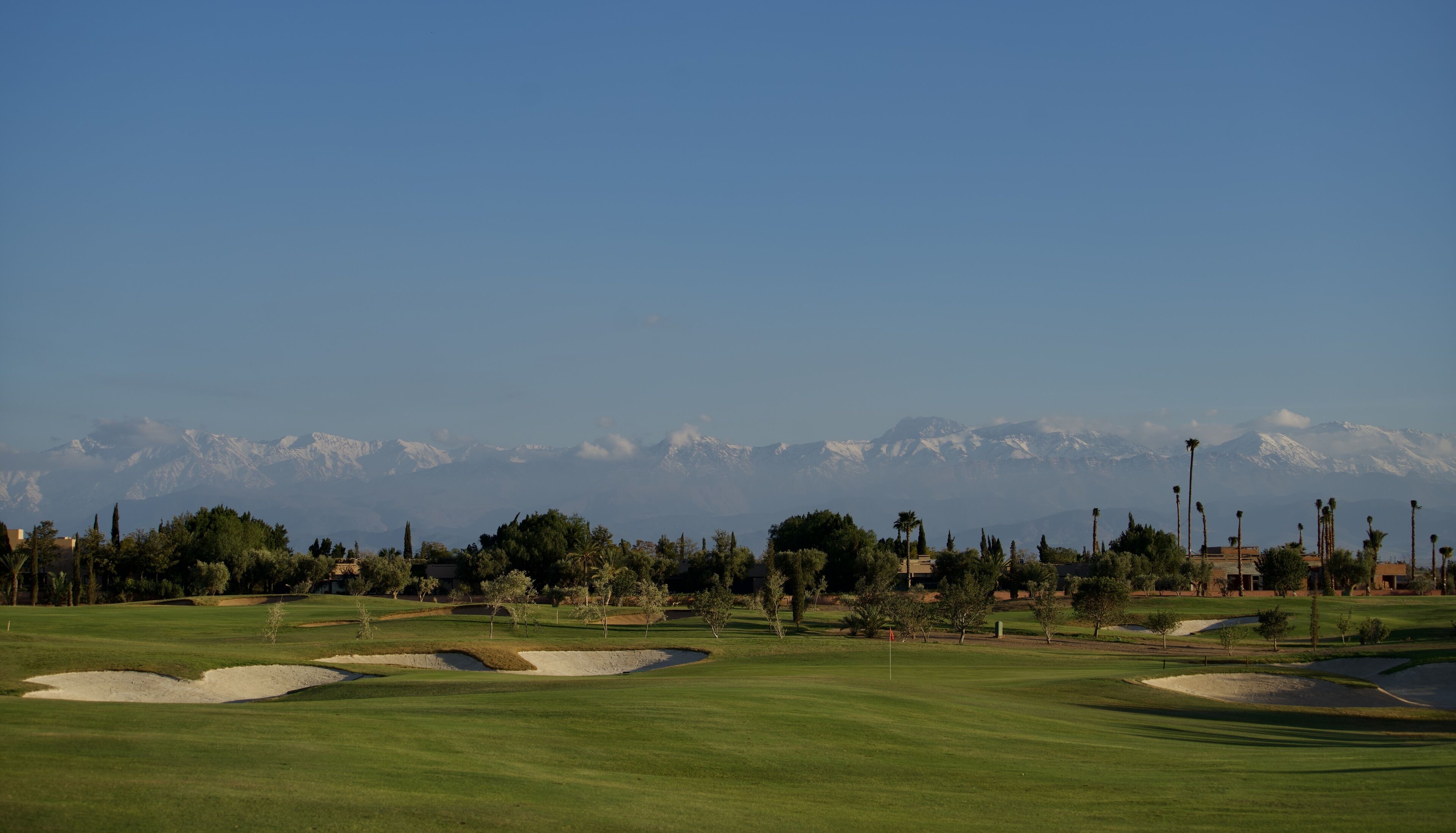 Ein Golfplatz mit freiem Blick auf schneebedeckte Berge im Hintergrund.