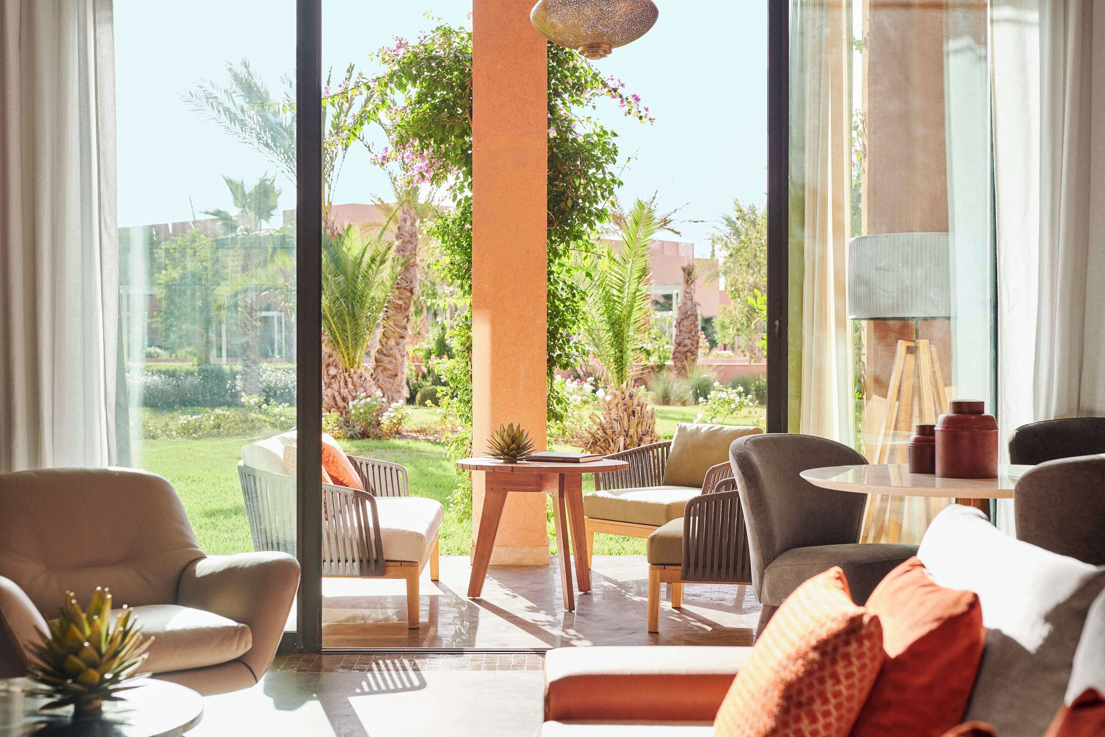Un salon moderne donnant sur un jardin, comprenant un canapé, des fauteuils, une table et une lampe.