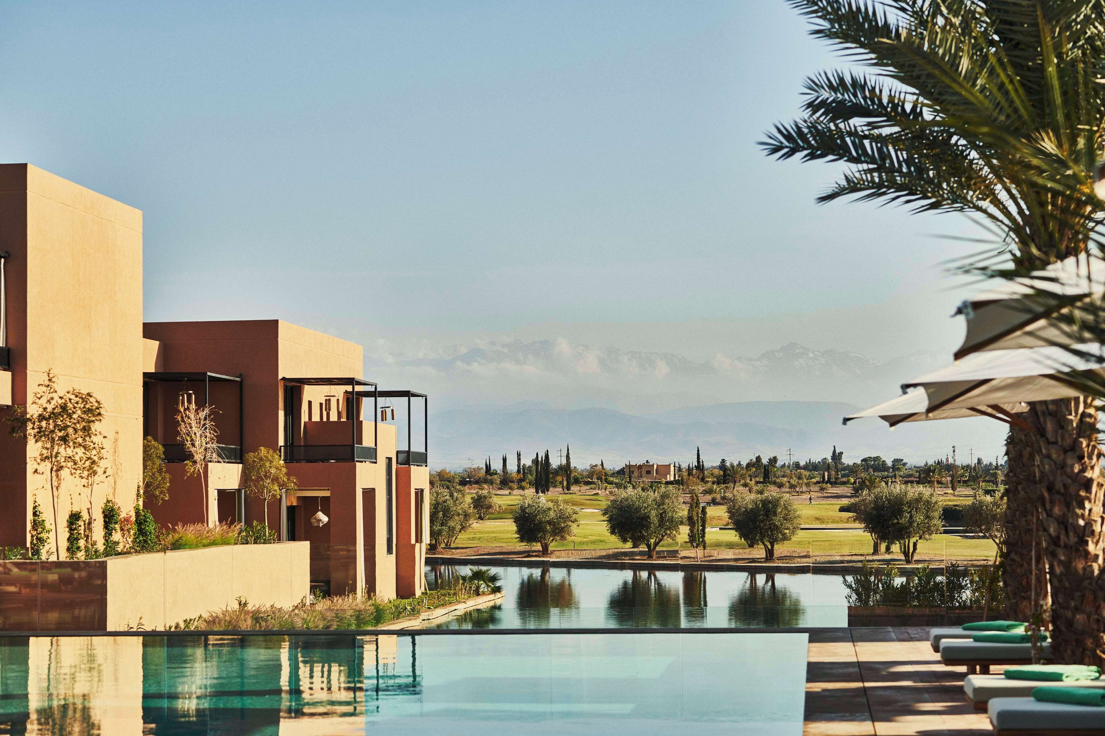 Ein modernes Hotel mit Pool, Bergblick und einem Golfplatz im Hintergrund.