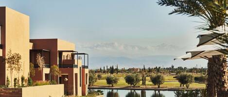 A modern hotel with a pool, a view of mountains, and a golf course in the background.