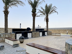 Un área de patio al aire libre con pared de piedra, una parrilla empotrada y palmeras.