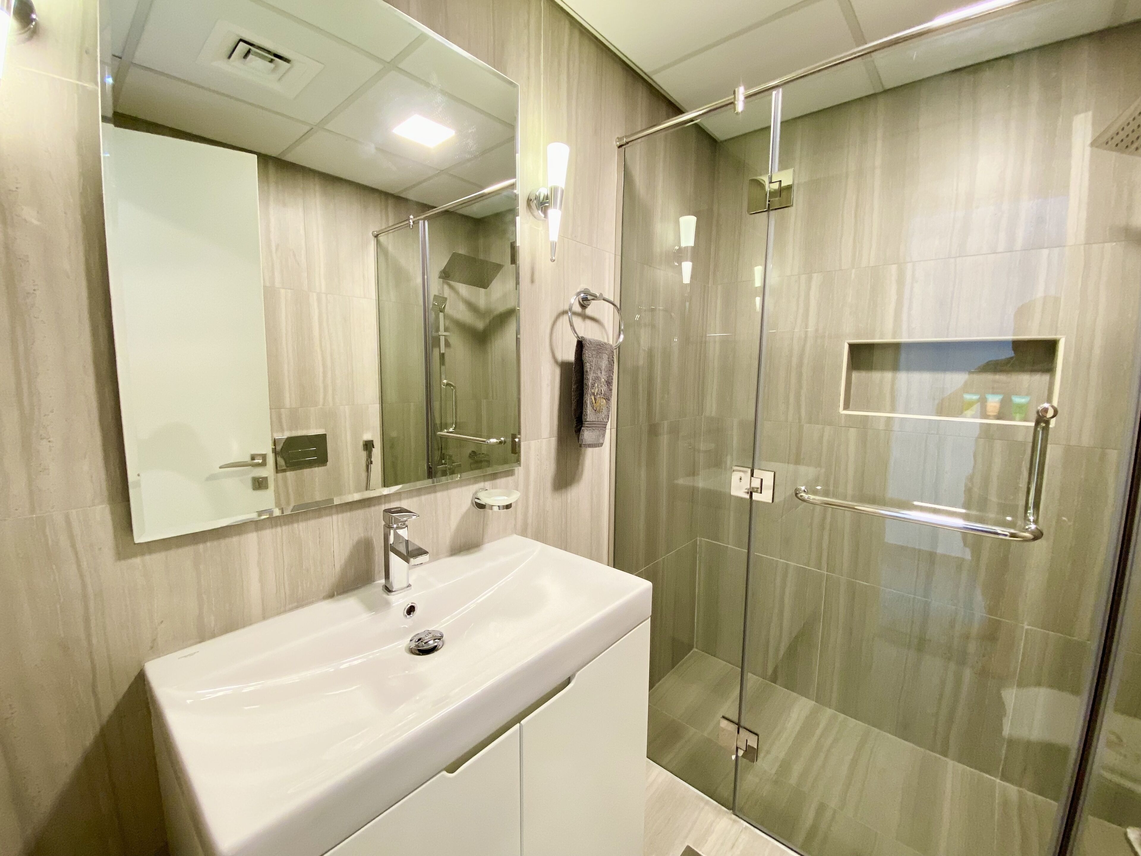 A modern bathroom with a large mirror, a white sink, a glass shower enclosure, and a towel rack.