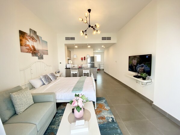 Una habitación de hotel moderna con cama, sofá, televisor y kitchenette.