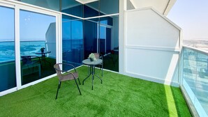 A balcony with a view of the sea, a small table with a chair, and artificial grass flooring. - Marco Polo - Pastel Studio with Stunning Aerial City Views (Dubai)
