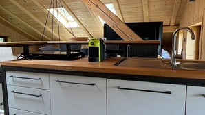 An attic kitchen with exposed wooden beams, a central island with a sink, and a window providing natural light.