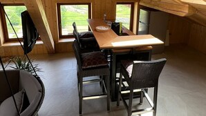 A wooden interior with a dining table, chairs, a hanging television, and large windows.