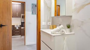 Een moderne badkamer met een witte wastafel, een spiegel en een kleine plant in een pot.