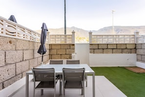 A patio with a table and chairs, a white fence, and a view of mountains.