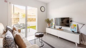 Een woonkamer met een bank, een televisie, een plafondventilator en een schuifdeur die leidt naar een buitenruimte.