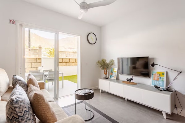 A living room with a sofa, a TV, a ceiling fan, and a sliding glass door leading to an outdoor area.