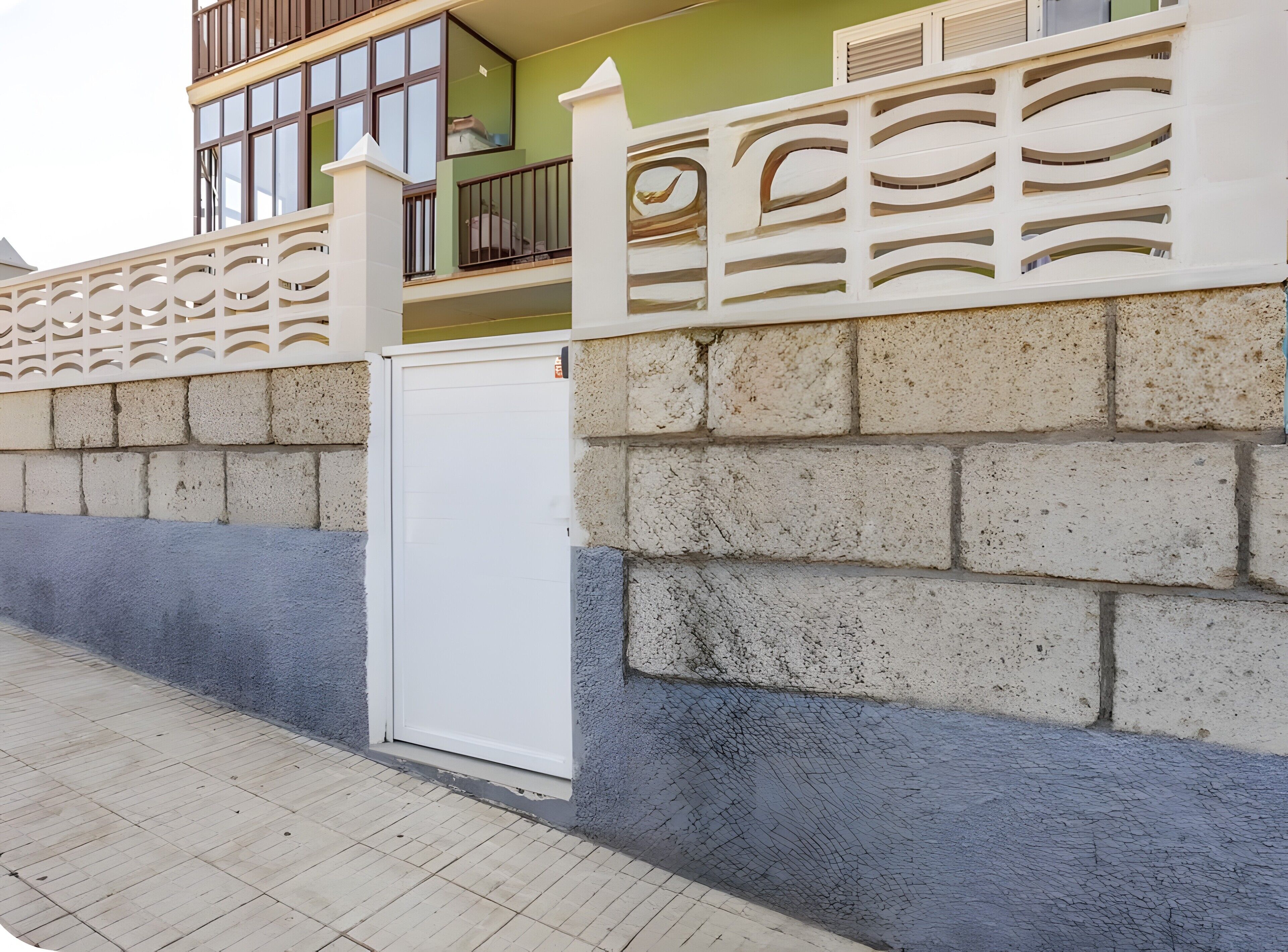 Un edificio con entrada porticada, un balcón con barandilla y un muro de hormigón.