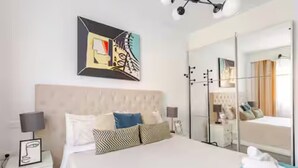 Een hotelkamer met een groot bed, een nachtkastje met een lamp, een spiegel en een schilderij aan de muur.
