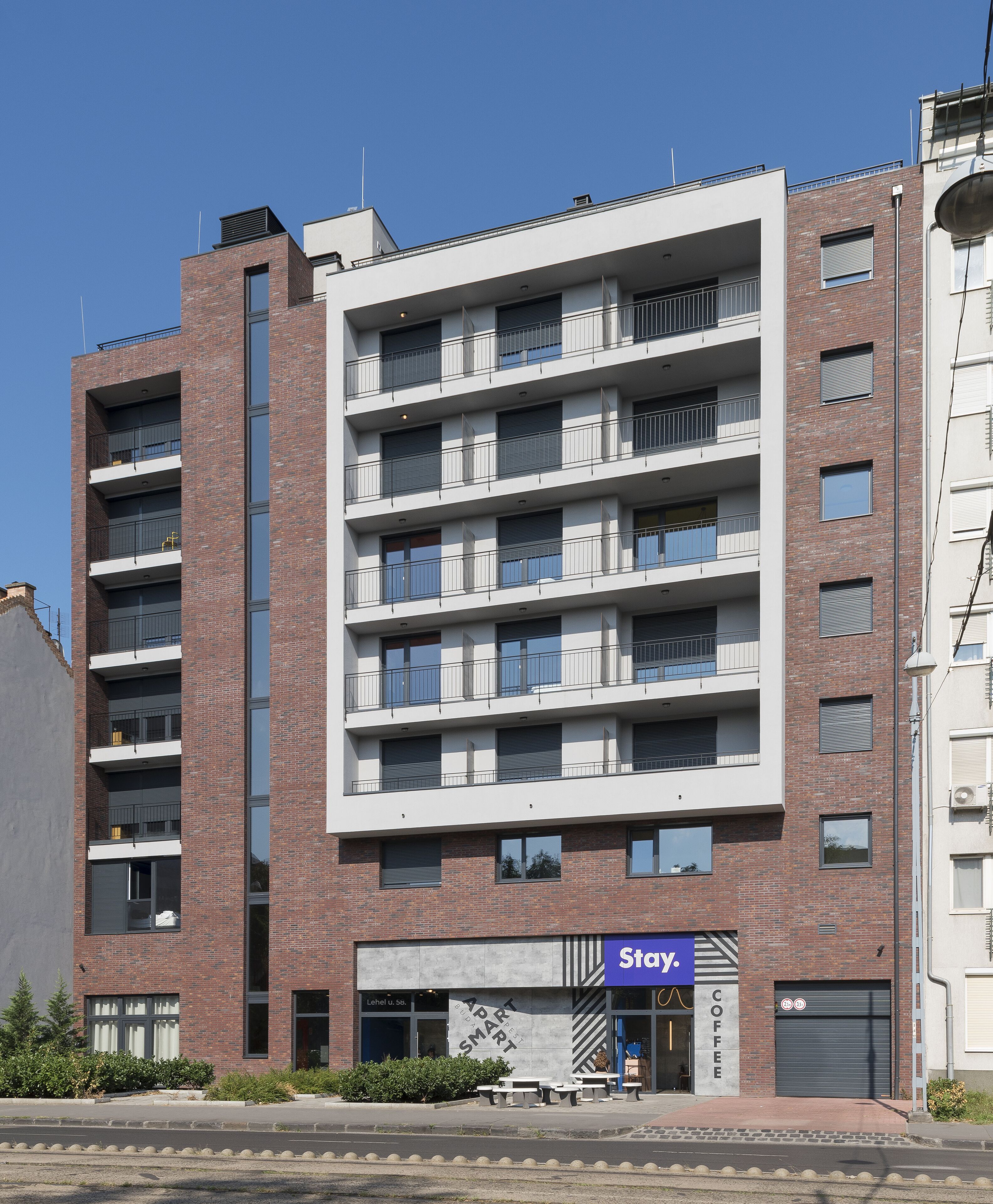 A multi-story building with a mix of brick and white facade, featuring balconies and a ground-level coffee shop named Stay.