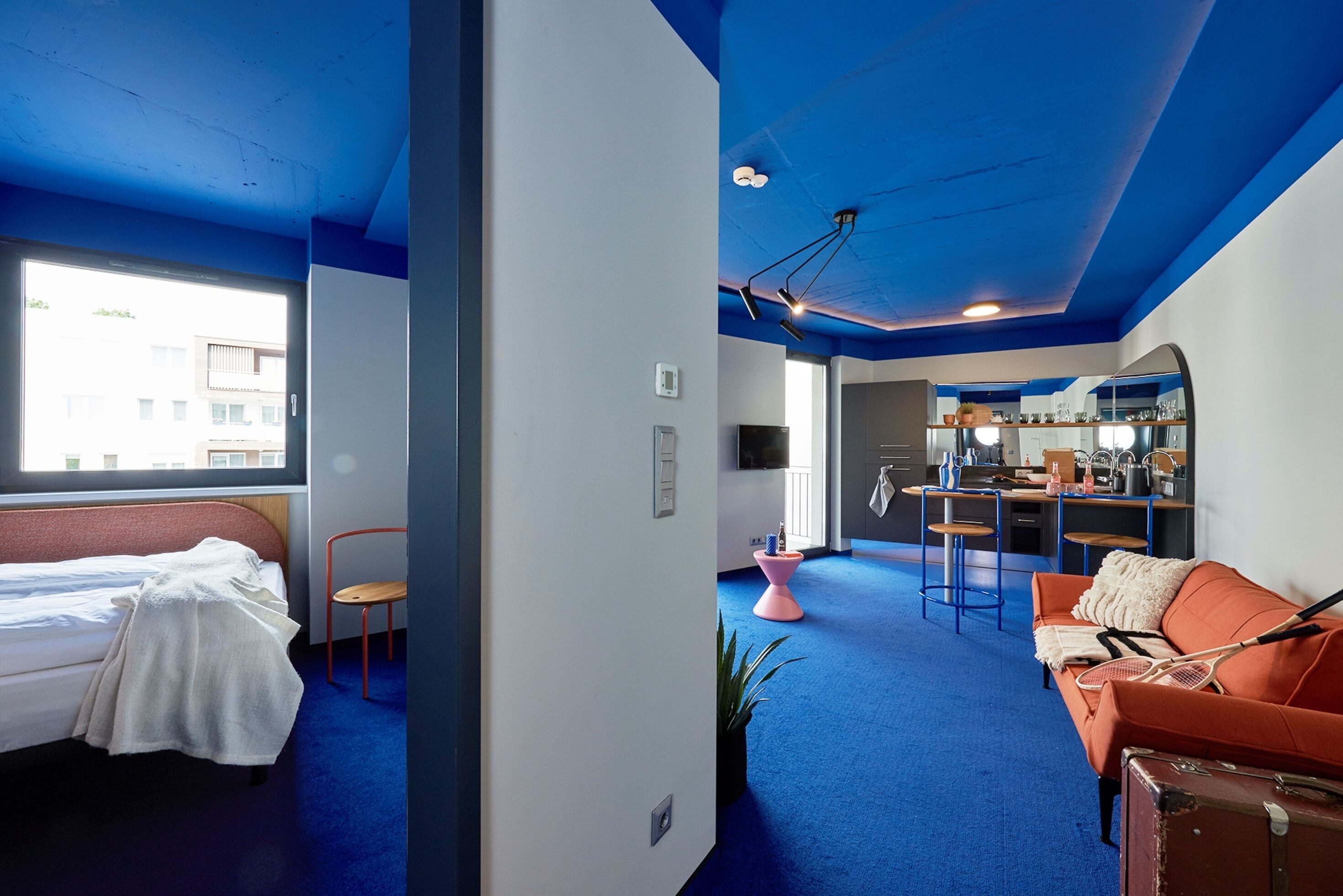 Een moderne hotelkamer met een bed, een bank, een zithoek met een bar en een groot raam met uitzicht.