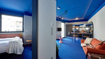 Een moderne hotelkamer met een bed, een bank, een zithoek met een bar en een groot raam met uitzicht.