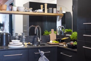 A modern kitchen with a black countertop, stainless steel sink, and a wooden shelf above.