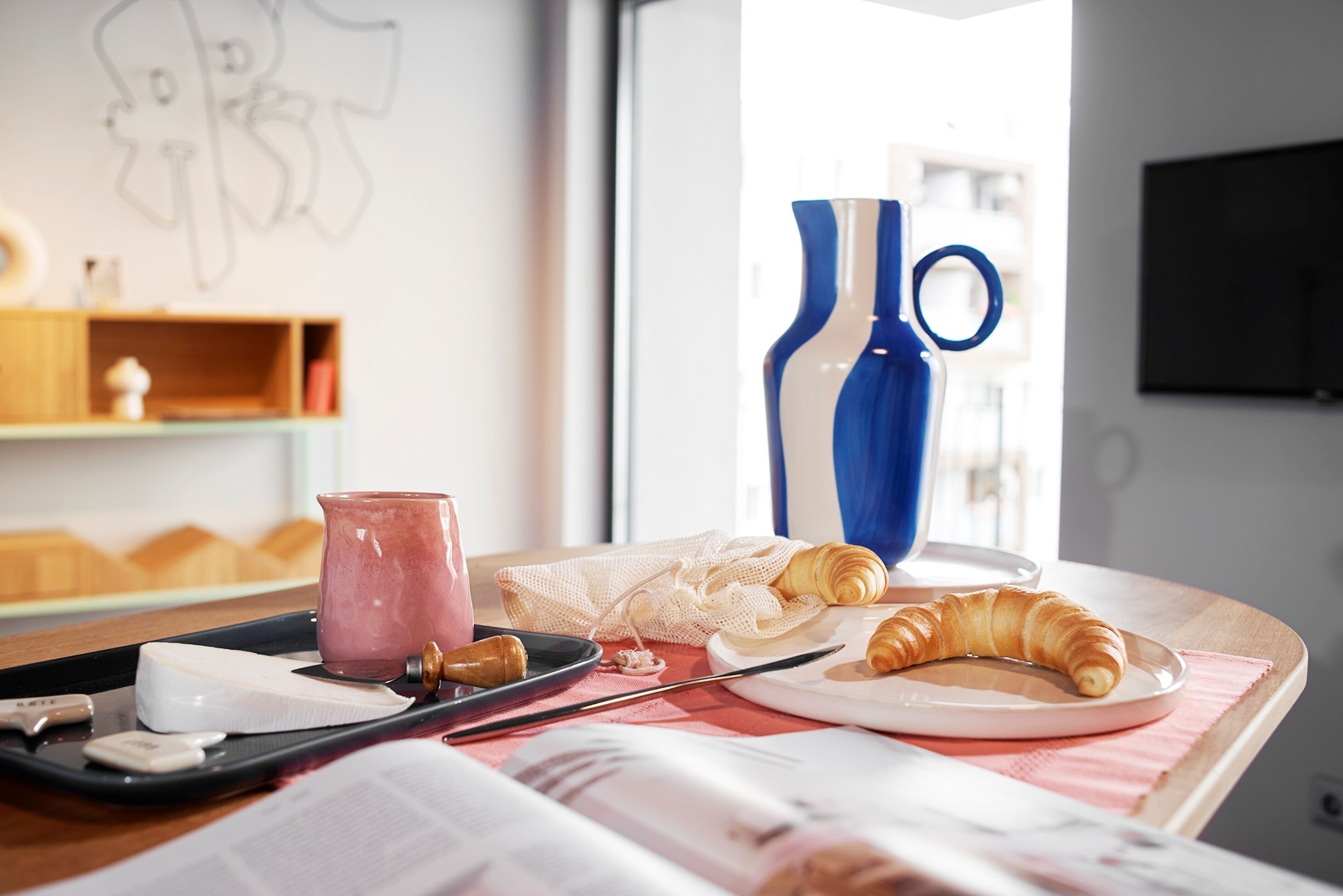 A breakfast setup with croissants, a croissant on a plate, a pink drink, and a book on a table.