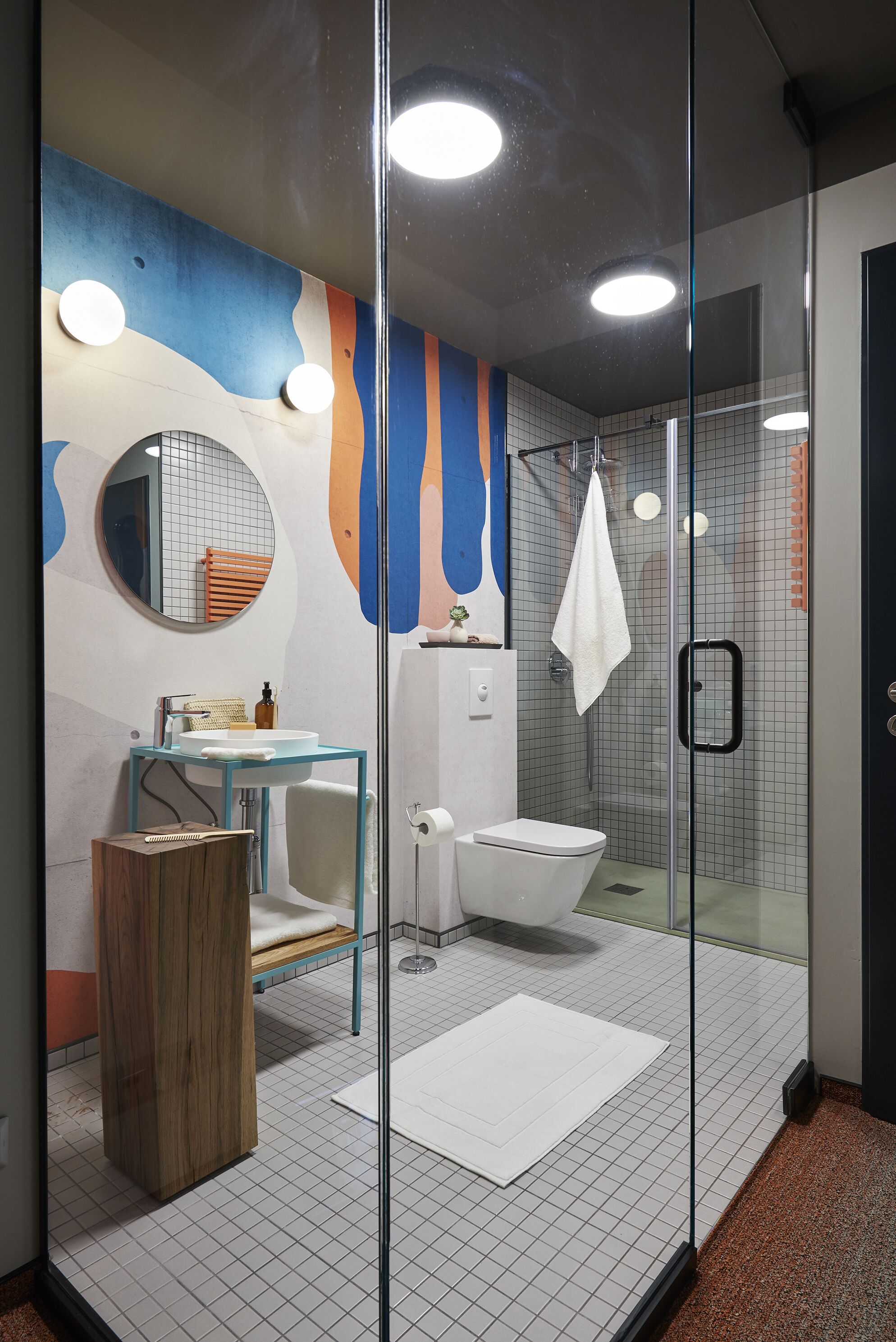 Un baño moderno con cabina de ducha de vidrio, un espejo redondo, un lavamanos blanco y un inodoro.
