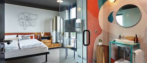 Un dormitorio moderno con un separador de vidrio, una cama, una mesita de noche, un espejo y un baño con lavamanos y toallero.